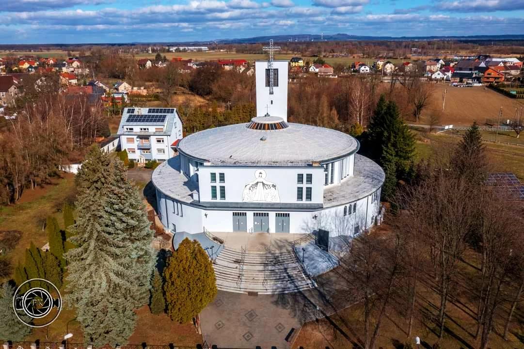 Kościół NMP Królowej Świata w Rogach z lotu ptaka, wśród zabudowy i drzew